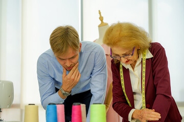 old caucasian fashion designer stylist with yellow measurement tape work with colleague man in...