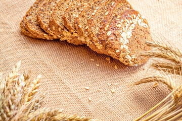 Sliced Multigrain. Rye bakery with crusty loaves and crumbs. Fresh loaf of rustic traditional bread with wheat grain ear or spike plant on natural cotton background. Bio ingredients, very healthy.