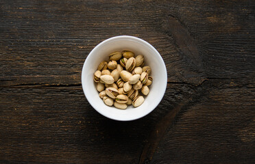 Pistachios in a small plate on a vintage wooden table. Pistachio is a healthy vegetarian protein nutritious food. Natural nuts snacks.