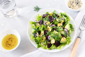 Healthy vegan salad of avocado, beetroot, greens and sesame in a white bowl. Top view