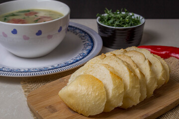 Caldo Verde Soup is a popular soup in Portuguese cuisine with greens and chopped chorizo on the top in ceramic bowl and piece of bread and pepper. Top View.