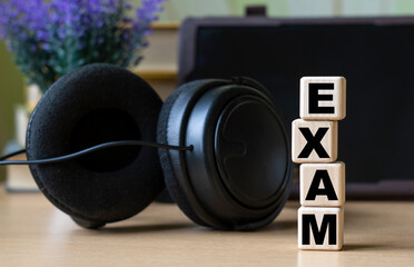 Fototapeta na wymiar EXAM -word on cubes on the background of the tablet, headphones and a white cup