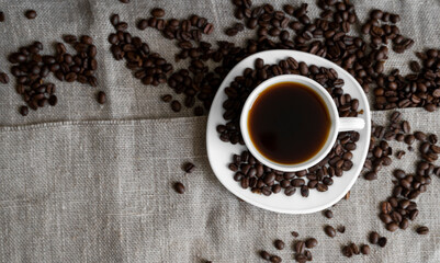 Coffee cup with roasted coffee beans on linen background. Mug of black coffe with scattered coffee beans. Fresh coffee beans.