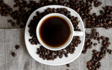 Coffee cup with roasted coffee beans on linen background. Mug of black coffe with scattered coffee beans. Fresh coffee beans.