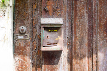 an old, worn, rusted and unlabeled mailbox, mounted on an old weathered wooden door. Next to it is an unlabeled bell.