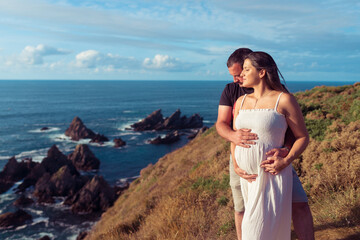 Fototapeta na wymiar Pregnant couple on top of a cliff near the ocean