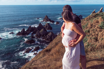 Fototapeta na wymiar Pregnant couple on top of a cliff near the ocean