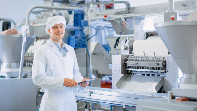 Young Male Quality Supervisor or Food Technician is Inspecting the Automated Production at a Dumpling Food Factory. Employee Uses a Tablet Computer for Work. He Looks to the Camera and Smiles.