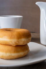 Two fresh donuts for breakfast on a wooden table, cup of espresso and jug of milk