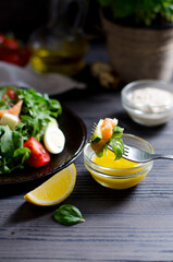 Forkful of salad in focus with vegetable and salmon salad in dark plate on blurred background, with sauces, vertical closeup on dark wooden table