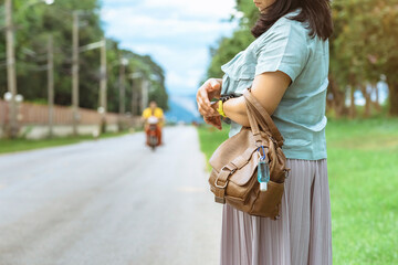 Mini portable alcohol gel bottle to kill Corona Virus(Covid-19) hang on leather shoulder bag of woman standing outdoor roadside.New normal lifestyle.Health care concept.Selective focus on alcohol gel