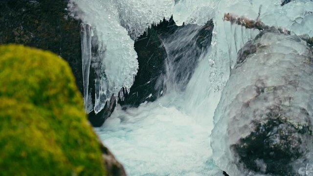 River with clear ice water with a waterfall, green moss and icicles on the rocks