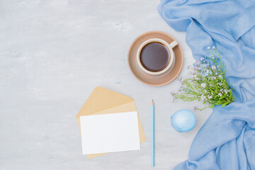 Mockup white greeting card, a cup of coffee and small blue flowers on a light background
