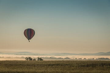 Obraz premium Hot Air Balloon floats over fog filled farm field and rolling hills at sunrise