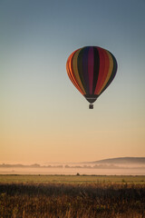 Fototapeta premium Hot Air Balloon floats over fog filled farm field and rolling hills at sunrise