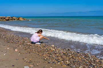 Little girl dressed in pastel colors jumping and playing on the stone and sandy shore of the Mediterranean Sea