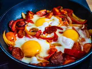Shakshuka - fried eggs with sausages and vegetables in frying pan