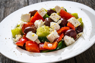 Fresh Greek salad - feta cheese, cherry tomatoes, lettuce, black olives and onion on wooden table