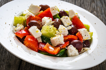 Fresh Greek salad - feta cheese, cherry tomatoes, lettuce, black olives and onion on wooden table