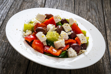 Fresh Greek salad - feta cheese, cherry tomatoes, lettuce, black olives and onion on wooden table