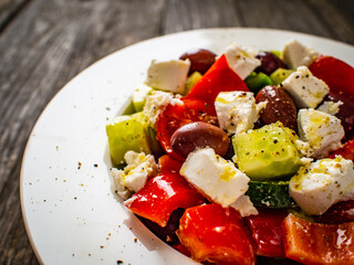 Fresh Greek salad - feta cheese, cherry tomatoes, lettuce, black olives and onion on wooden table