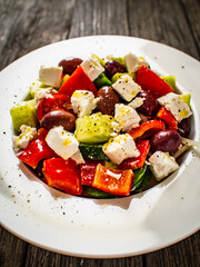 Fresh Greek salad - feta cheese, cherry tomatoes, lettuce, black olives and onion on wooden table