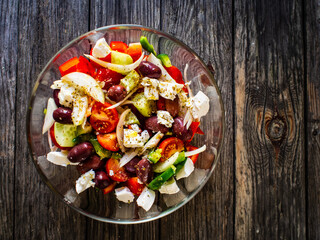 Fresh Greek salad - feta cheese, cherry tomatoes, lettuce, black olives and onion on wooden table