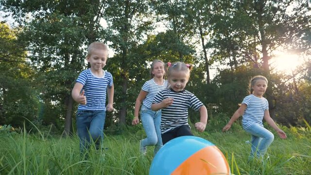 Happy Family Of Children Has Fun In The Park. Children With A Crowd Run For A Colorful Ball, Catching Up. Kids At Sunset In The Park Have Fun Playing. Team Game Girls And Boy.