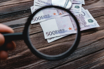 Magnifying glass on pile of Euro banknotes as Euro economy or debt analysis concept. Tax payment season concept or investment solutions. Searching a job with high salary