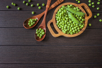 peeled green peas in a wooden plate and spoons top view. background with green sweet peas. green peas are cleaned and in the pod.