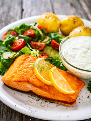 Fried salmon steak with potatoes and vegetables served on black plate on wooden table