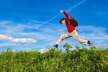 Back to school - young boy jumping, running against blue sky
