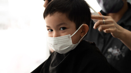 Cute little Asian boy  with protective mask and barber man or parent with protective mask doing a...