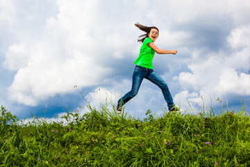 Fototapeta na wymiar Girl jumping, running against cloudy sky