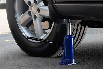 The blue hydraulic bottle jack is installed under the machine and lifting it.
