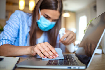 Woman is cleaning laptop by alcohol spray. Woman in the office using disinfectant for sanitizing monitor surface during COVID-19 pandemic. Coronavirus. Sanitizer. Woman working in quarantine.