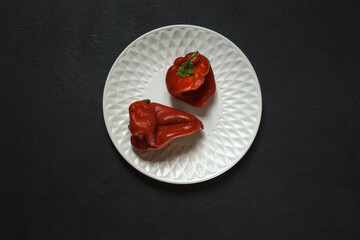 Two shriveled red peppers on a round white plate. Black background with space, horizontally