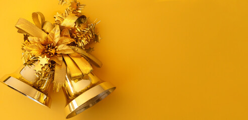Gold Christmas bells with ribbons and poinsettia on a yellow background with copy space. Close-up, top view, horizontal position, banner