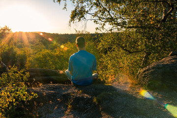 Young man sitting on stone and looking to Czech ore mountain valley at sunset landscape