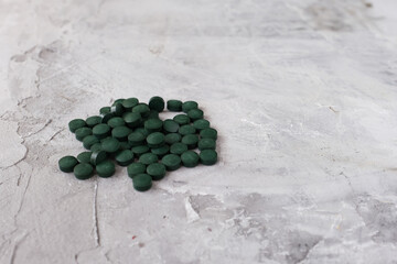 Green chlorella tablets on gray concrete background. Chlorella is a single-celled green algae, it is used to make nutritional supplements and medicine. Side view, selective focus, copy space.