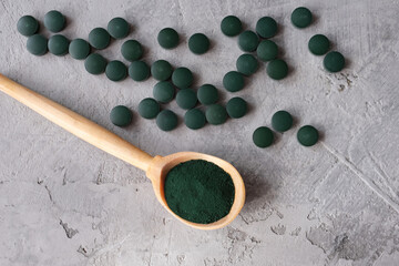Green chlorella powder in wooden spoon and green chlorella tablets on gray concrete background. Chlorella is a single-celled green algae, it is used to make nutritional supplements and medicine. Top v