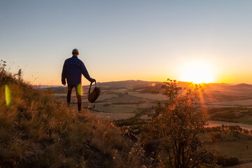 Young man standing on hill and hold backpack looking to Czech ore mountain valley at sunset landscape