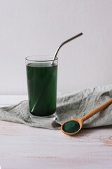 Green drink made from single-celled green algae chlorella and green chlorella powder in wooden spoon. Superfood detox in a glass, with reusable stainless steel straw on a white background.