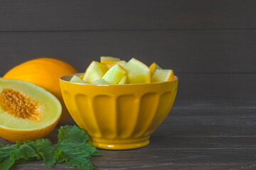 slices of sliced melon in a yellow bowl close-up on the table. background with a ripe melon.