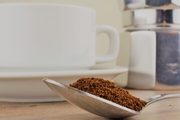 Coffee in a spoon on a wooden table, coffee maker and white cup in the background