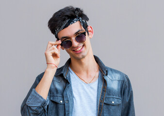 Confident in his perfect style. Handsome young fashionable man adjusting his sunglasses and looking at camera while standing against gray background