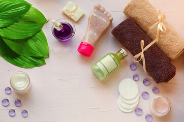 Fototapeta na wymiar Green fresh leaves on the background of organic cosmetics. Towels, cotton pads, pink cream, green gel, handcrafted soap, natural, foot care, pedicure, healthy feet