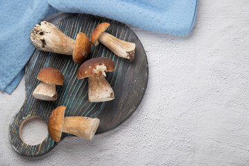 Fototapeta premium Forest porcini mushrooms lie on a round wooden cutting Board, on a light background. Russian cuisine.Horizontal orientation. Place for copy space