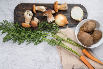 Fototapeta na wymiar Various ingredients for cooking various dishes from forest porcini mushrooms on a light background-mushrooms, carrots, potatoes, onions, with a wooden cutting Board. Horizontal . Place for copy space