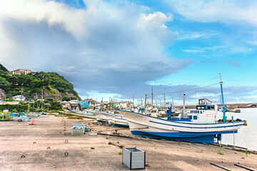 Fototapeta na wymiar Fishing boats moored on the port of the Kanaya village in Futtsu city along the Uraga Channel with the cliffs of the Mount Nokogiri stone quarry in the Boso peninsula.